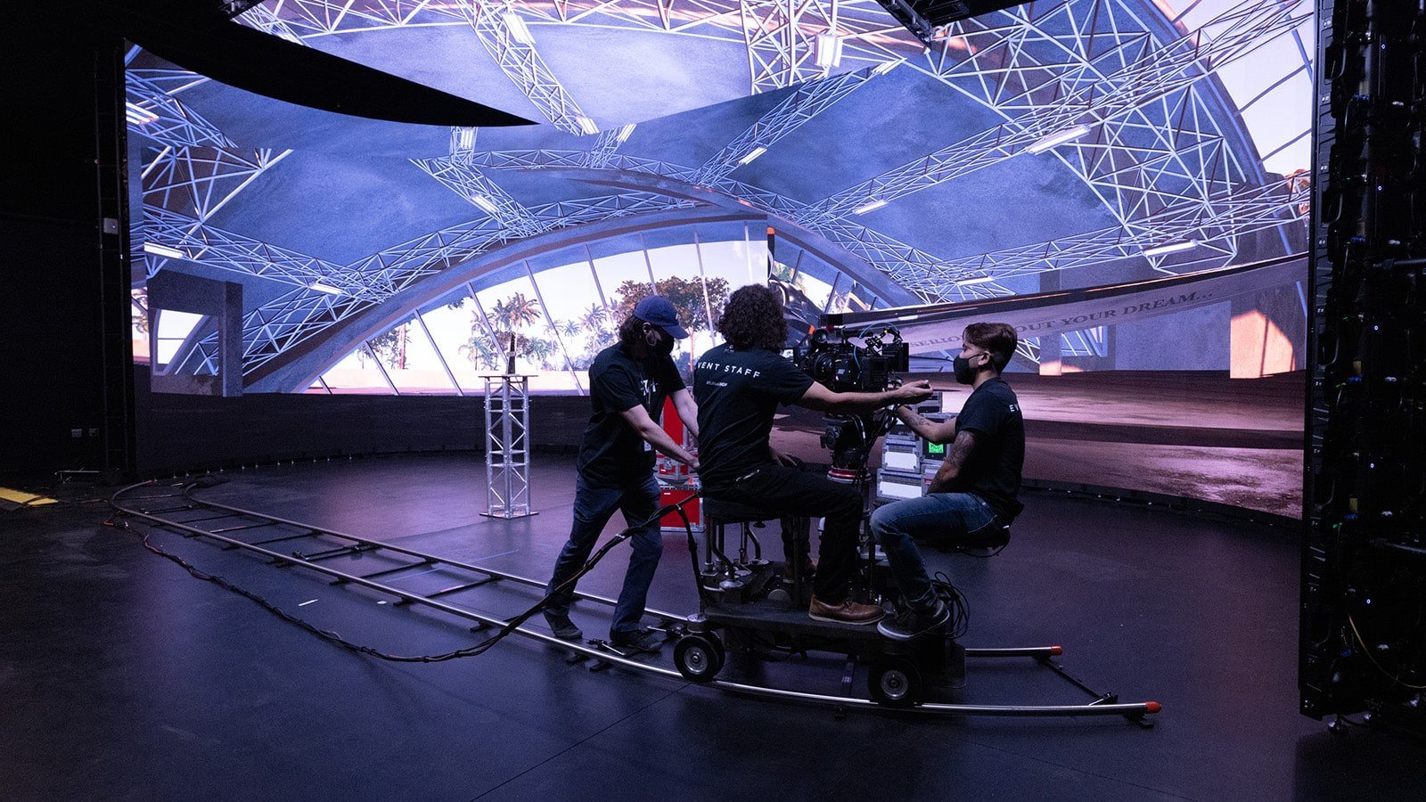 Crew members work on a dolly-mounted camera. A virtual production LED screen displays the interior of an airplane hangar