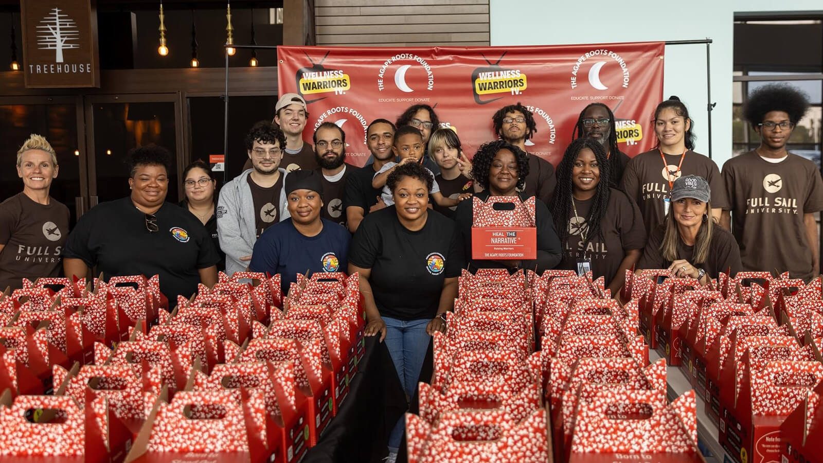 Full Sail volunteers and members of the Agape Roots Foundation pose with dozens of "Thrive Pack" care packages.