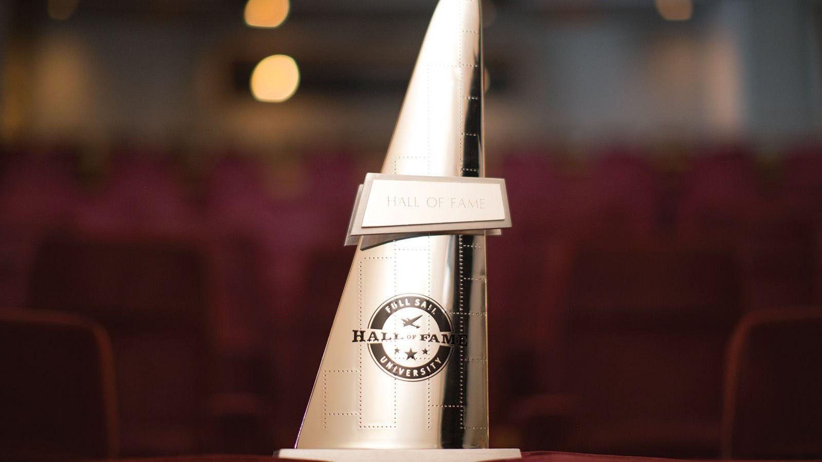 A gold, triangular statuette with the words Hall of Fame overlaid on the Full Sail University logo.