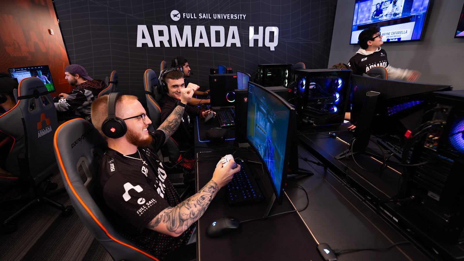 Gamers compete at Full Sail’s Armada HQ, celebrating a win in a high-energy esports match surrounded by teammates and gaming stations.