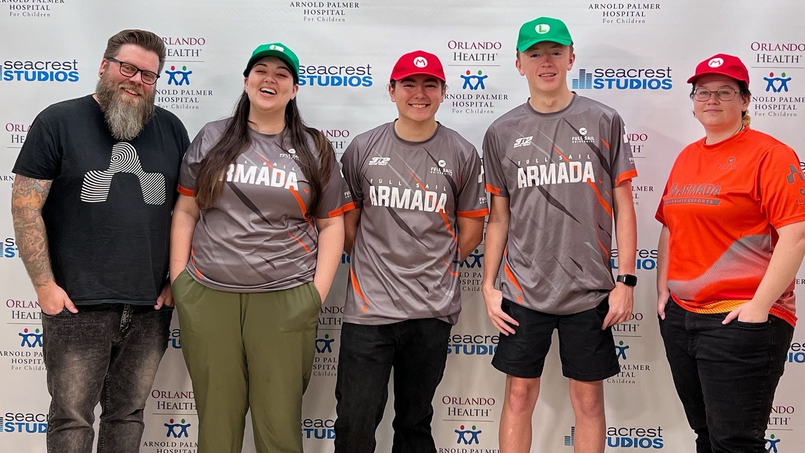 Five people posing in front of a “Seacrest Studios” backdrop, wearing Armada jerseys and hats, smiling at the camera.