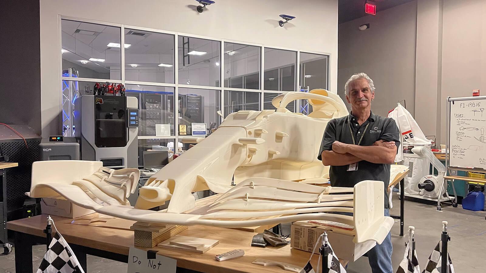 Course Director Pat Starace, a man with white hair and a grey polo shirt, standing next to a large workbench with a 3D-printed replica of a Formula 1 race car in Full Sail’s SimLab.