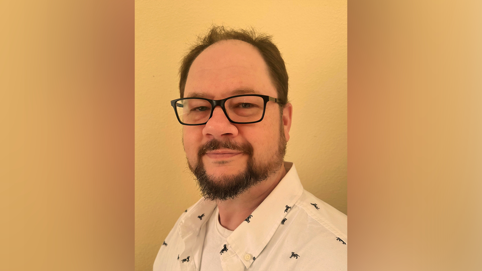 A shoulder-length photo of Sean wearing black-rimmed glasses and a white shirt.