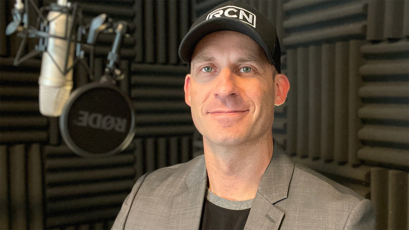 Phil Ellering stands in a podcast recording booth. He is wearing a black baseball cap with an RCN logo.