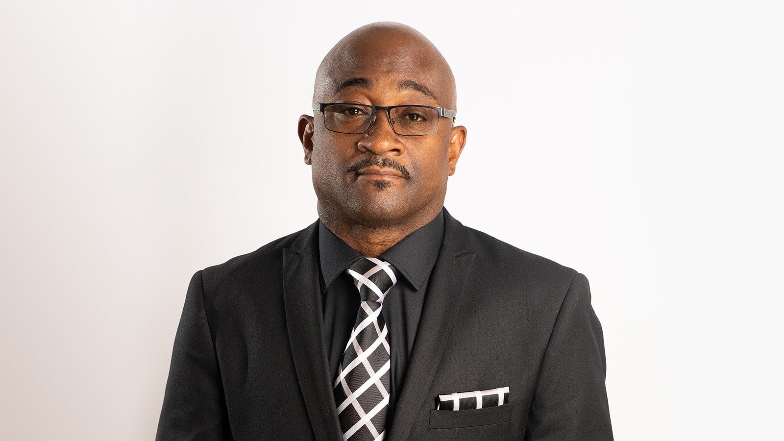 A headshot of Christopher Rapley wearing glasses and an all-black suit with a black-and-white tie and pocket square.