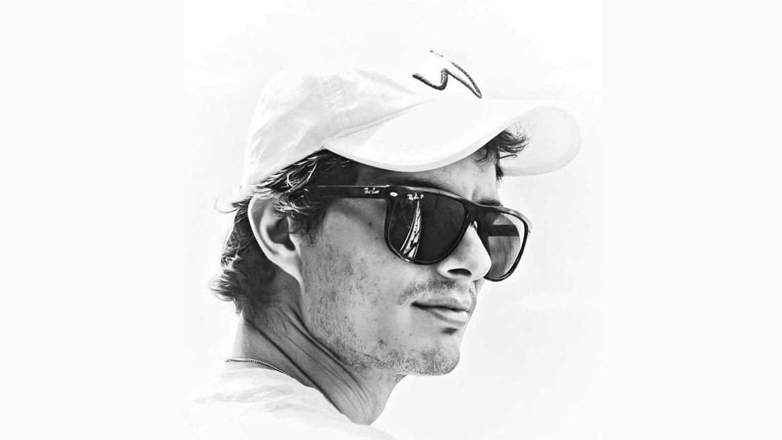 A black and white photo of Matias from the neck up, wearing a pair of sunglasses with dark frames while looking into the distance.