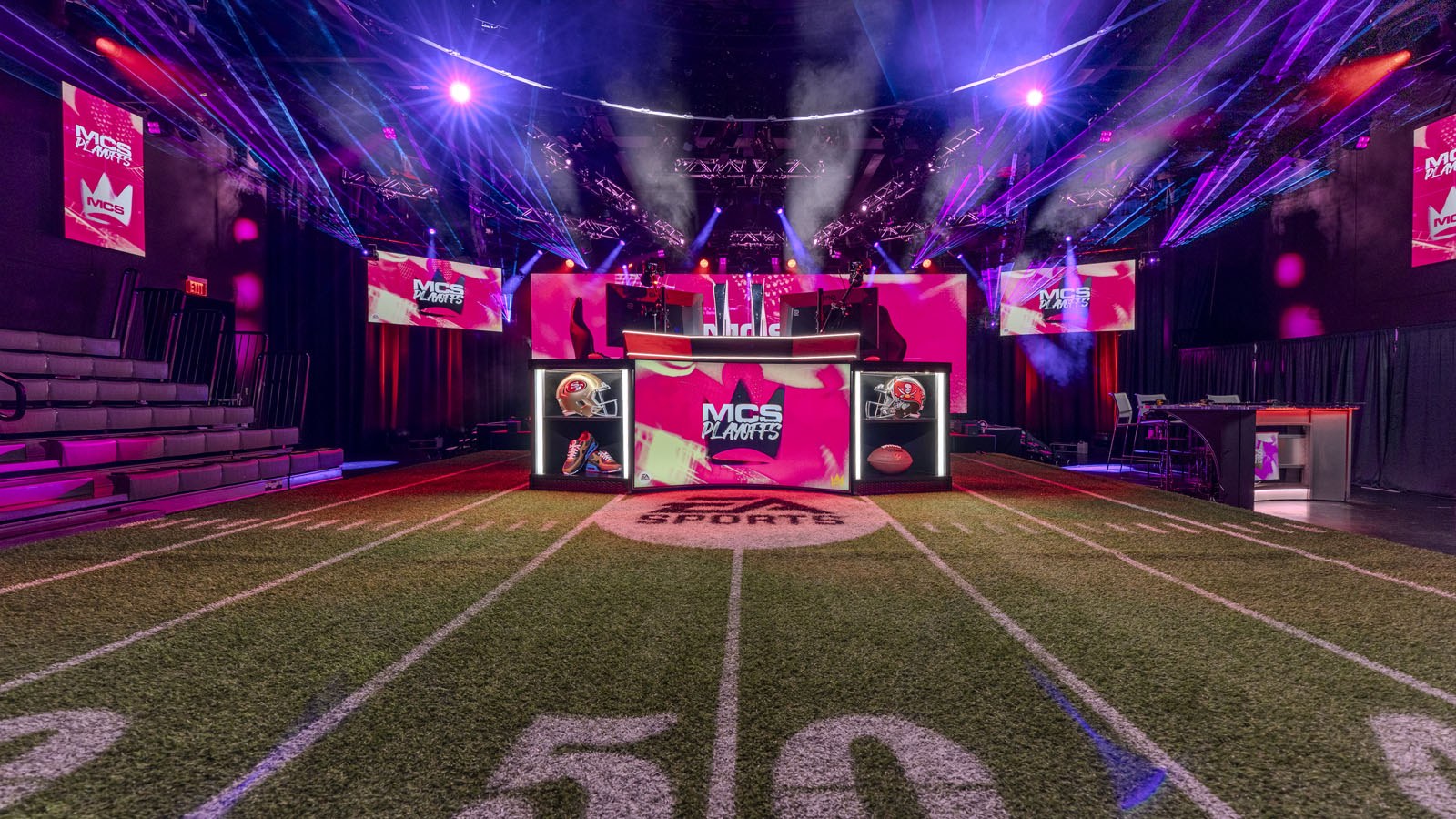 A vibrant esports stage with a football-themed setup, featuring "MCS Playoffs" branding, LED screens, and dynamic lighting.