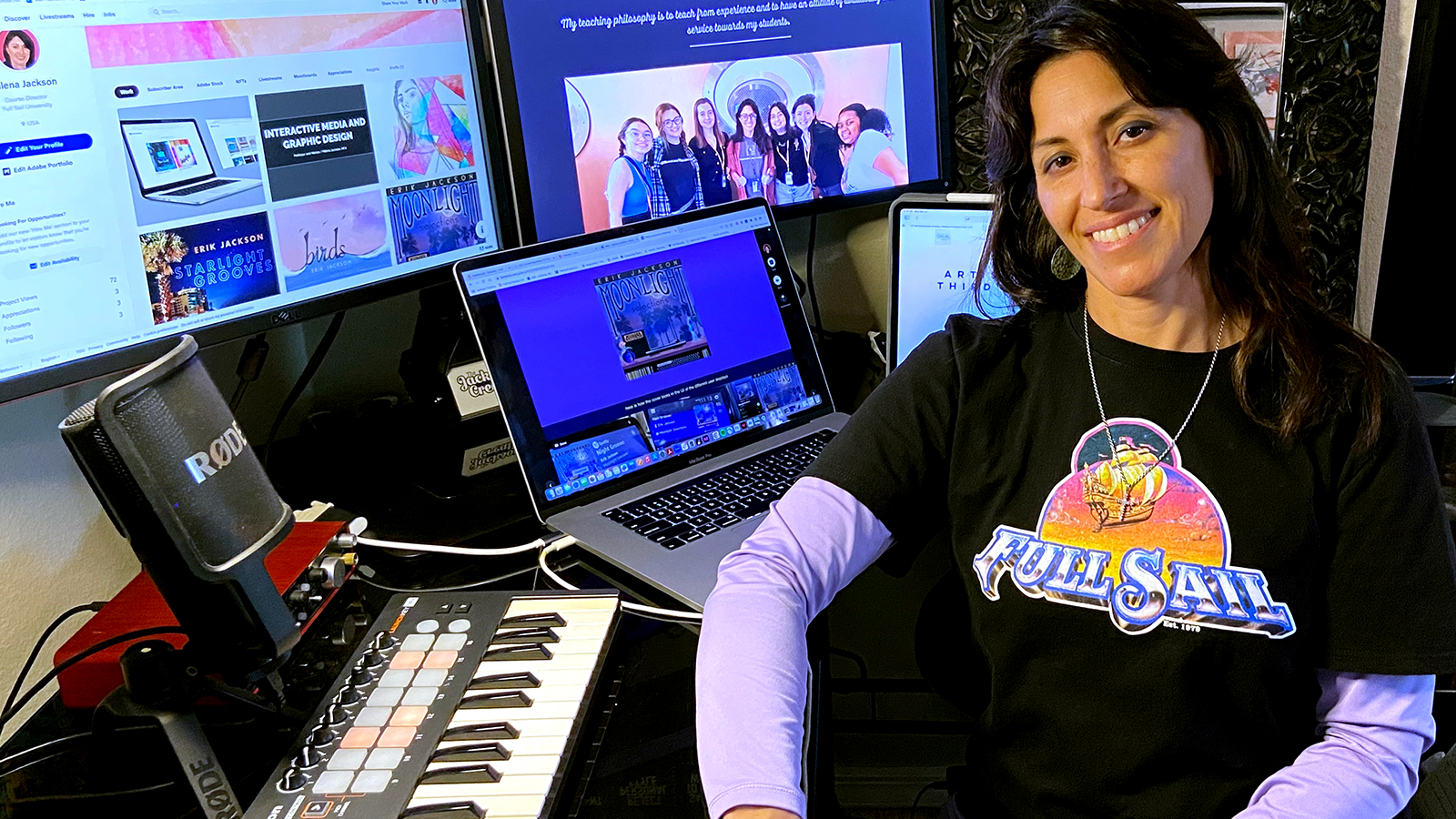 Instructor Milena Jackson, a woman with shoulder-length dark hair, is seated at her desk while wearing a Full Sail University graphic tee.