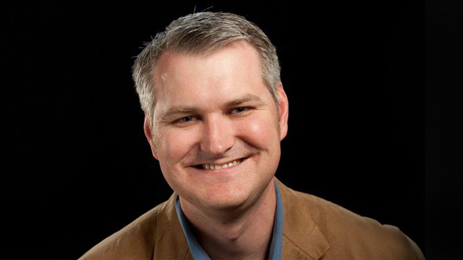 Eric Rosenfeld smiles at the camera. He has gray hair and is wearing a blue collared shirt with a tan blazer.