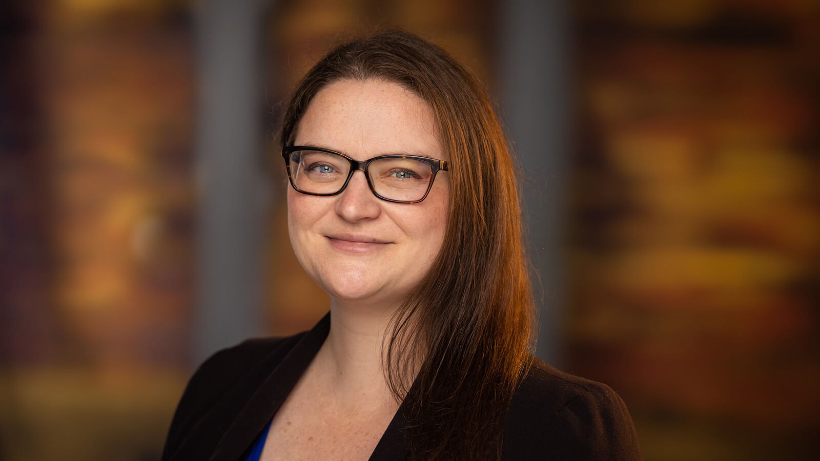 Rebecca Leis has brown hair and is wearing tortoiseshell glasses and a black blazer. She is smiling.