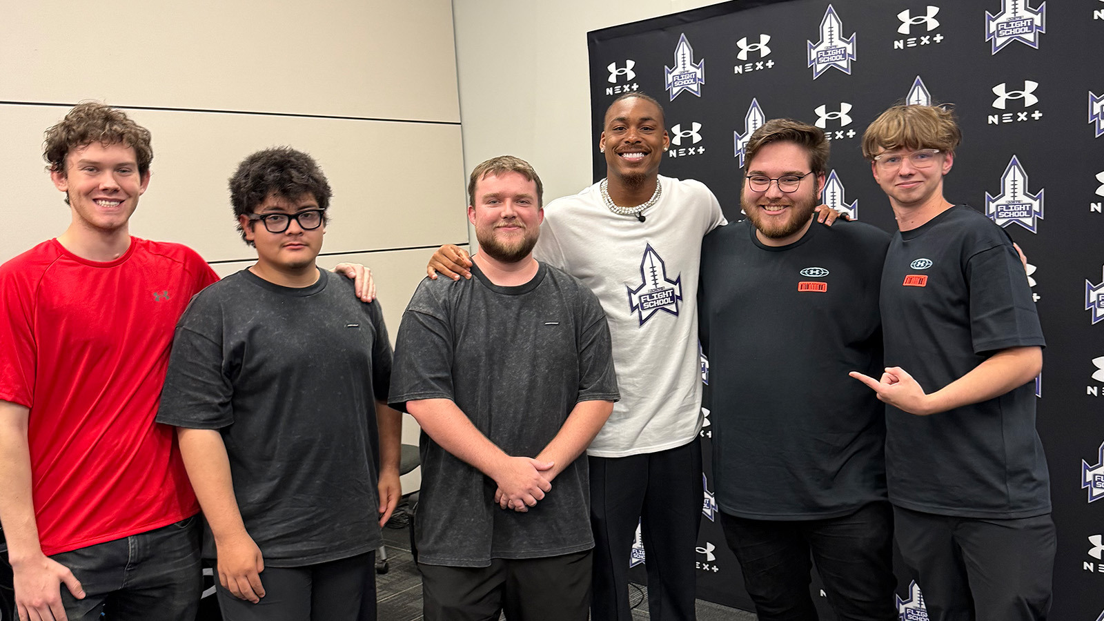 A group of five students, staff, and grads pose for a photo with NFL wide receiver Justin Jefferson in front of a step and repeat.