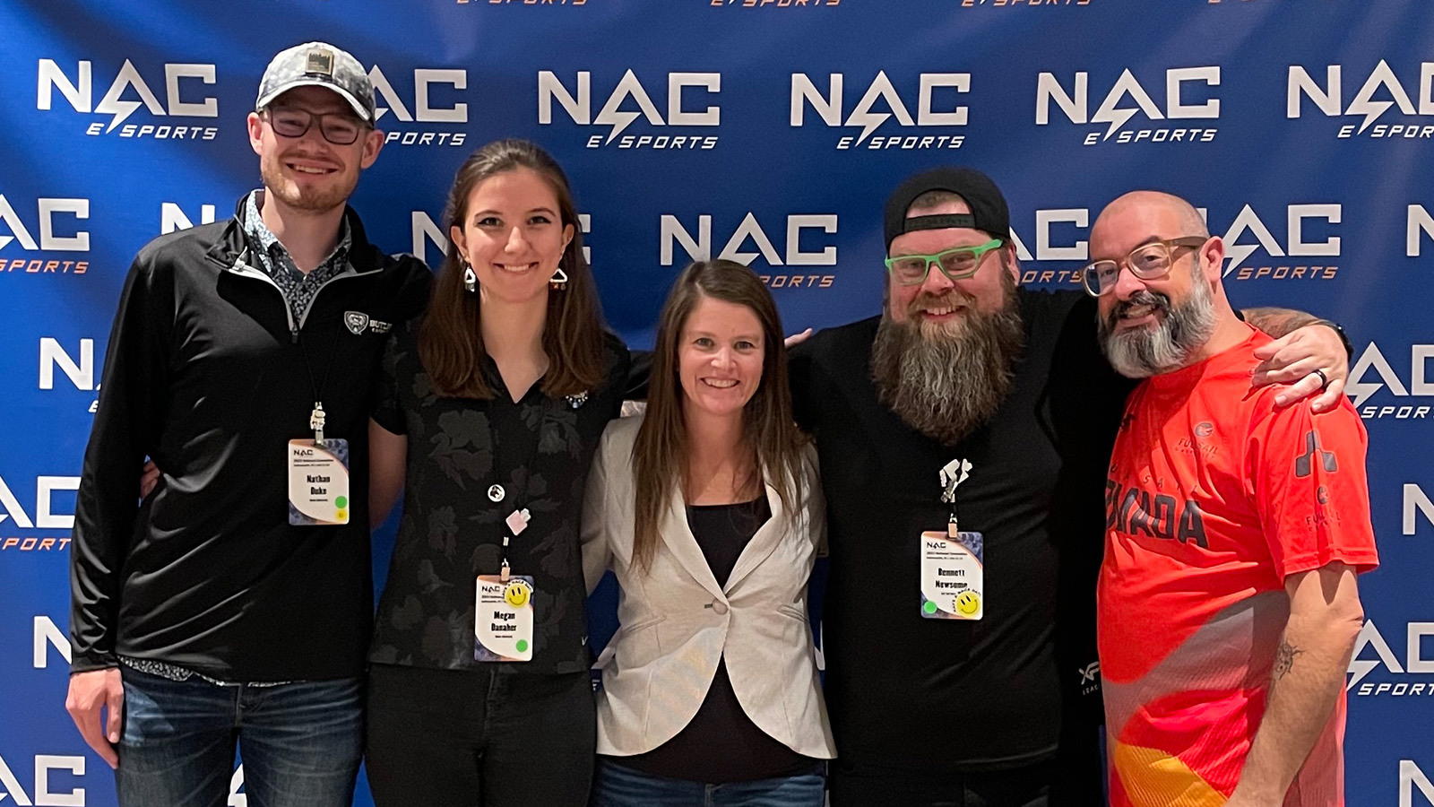 Armada graduates Nathan Duke and Megan Danaher and Full Sail esports staffers Sari Kitelyn, Bennett Newsome, and Jacob Kaplan stand in front of a NACE backdrop.