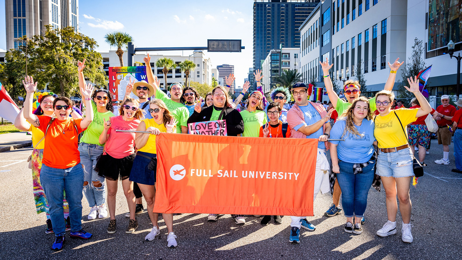 A group of Full Sail faculty, students, and staff posing with a large orange banner that reads “Full Sail University”