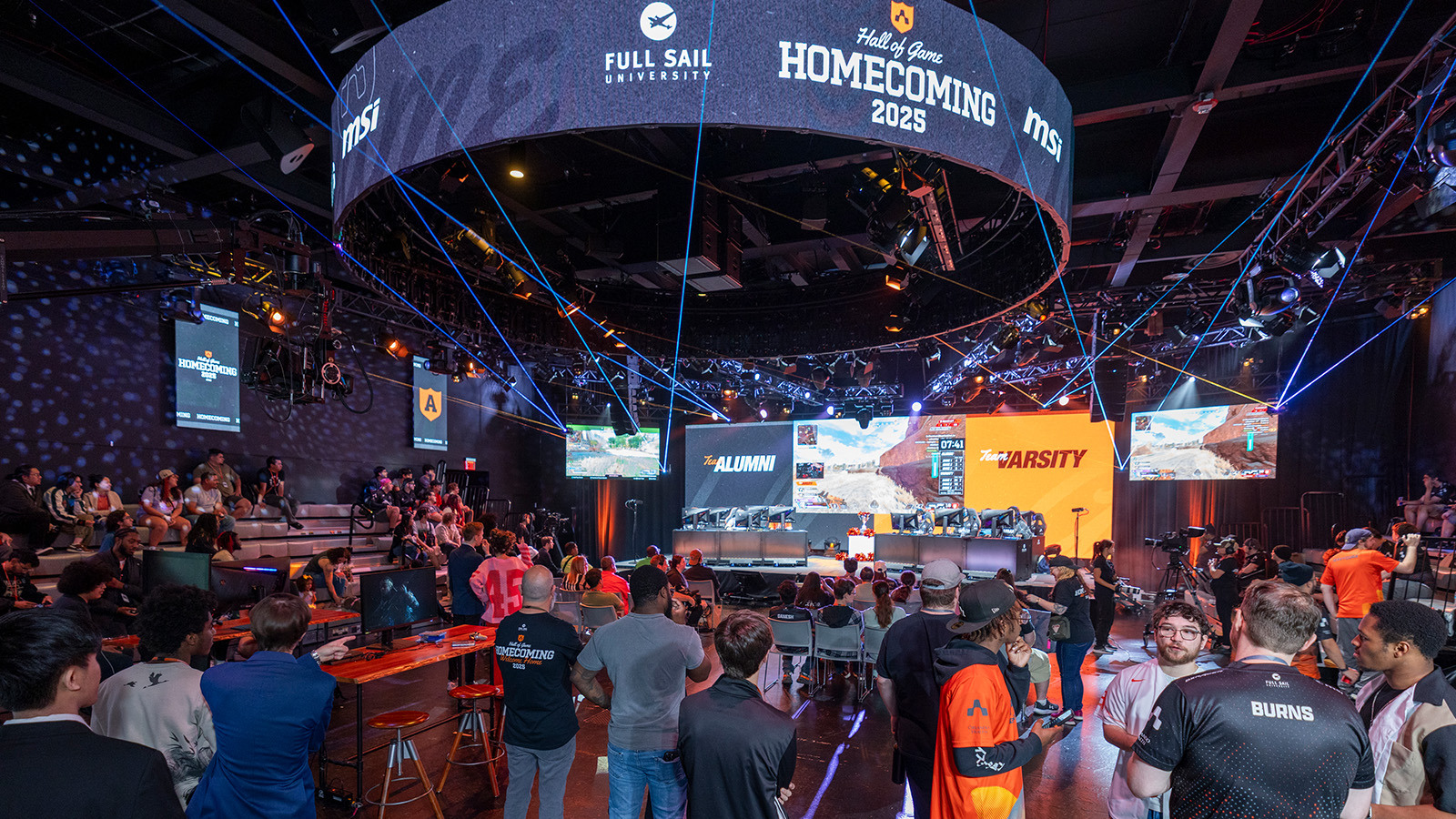Students and alumni gather in the Fortress as Armada Varsity and Alumni team members compete. Screens show the Hall of Game: Homecoming logo.