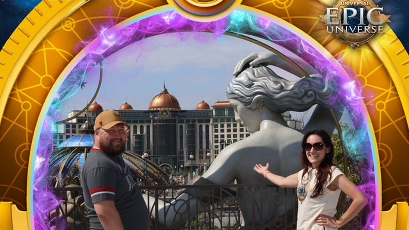 A man and woman stand together in front of an attraction featuring a large statue of a woman, a building with a glass dome, and a building with bronze domes.