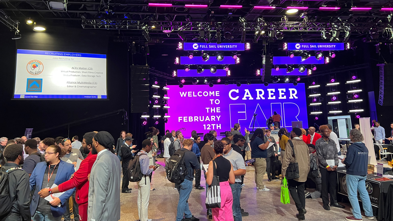 Students, alumni, and employers gather at the Full Sail Live venue for a career fair. A screen says, “Welcome to the February 12th Career Fair.”