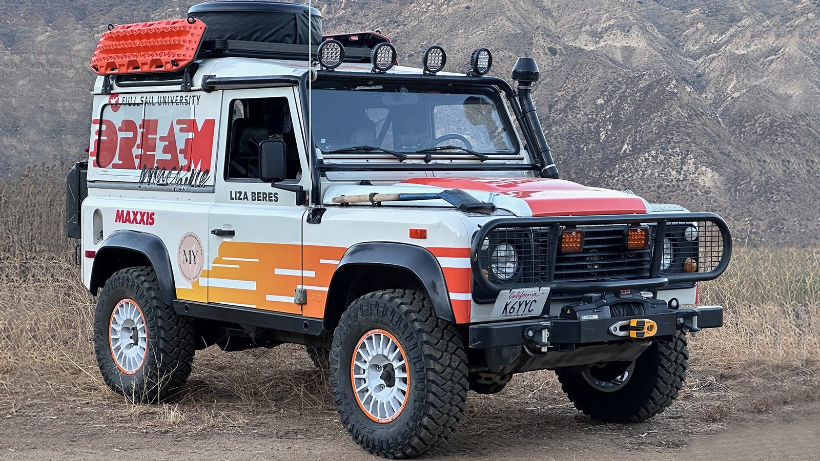 A Land Rover with the Full Sail logo and orange and white graphics is parked on a mountain trail.