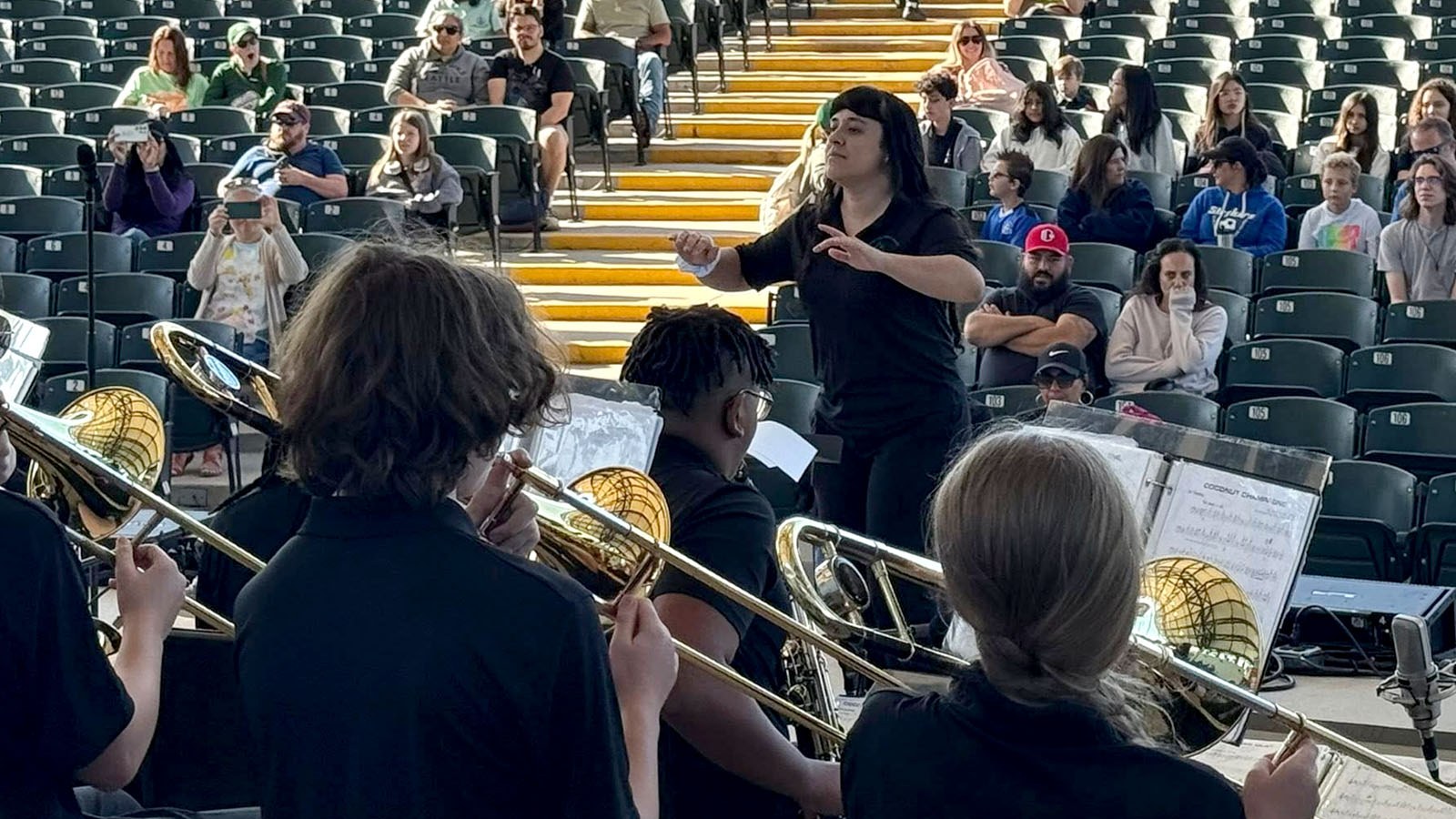 Students perform in a brass ensemble as a conductor leads, while audience members are seated in an amphitheater with Full Sail University tents in the background.