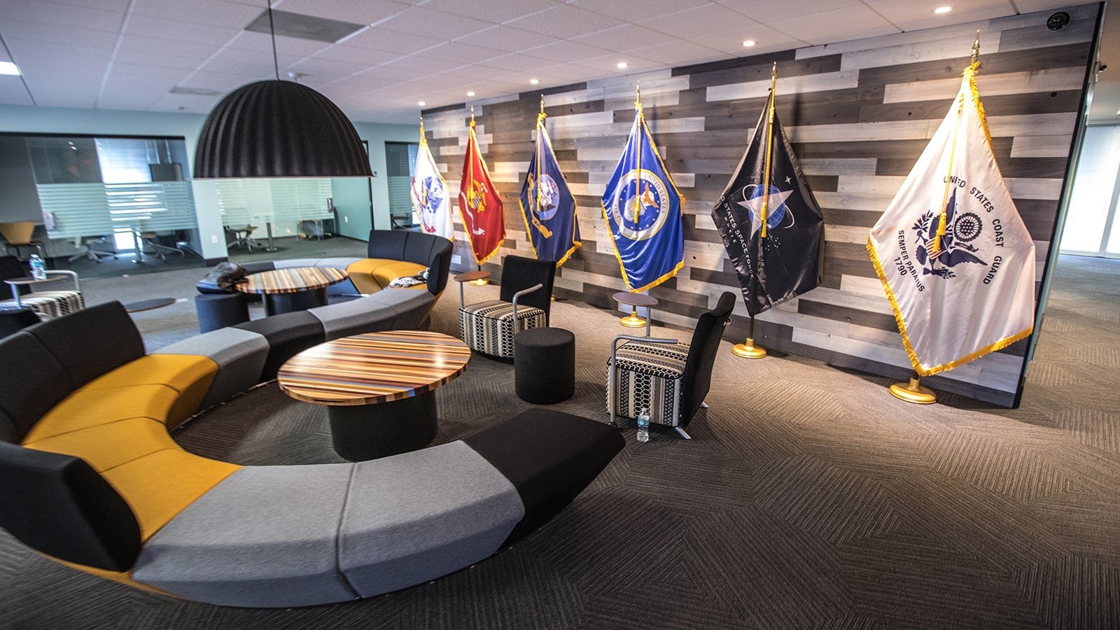 An image of Full Sail’s Military Student Success center shows a large couch, small meeting rooms, and flags representing each branch of the US Armed Services.