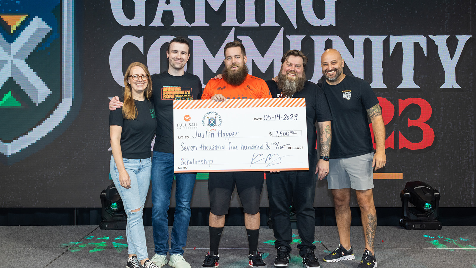 Sam Lupo, DrLupo, Bennett Newsome, and Kevin Murray on stage in the Fortress with a student in an orange Armada jersey receiving an oversized scholarship check.