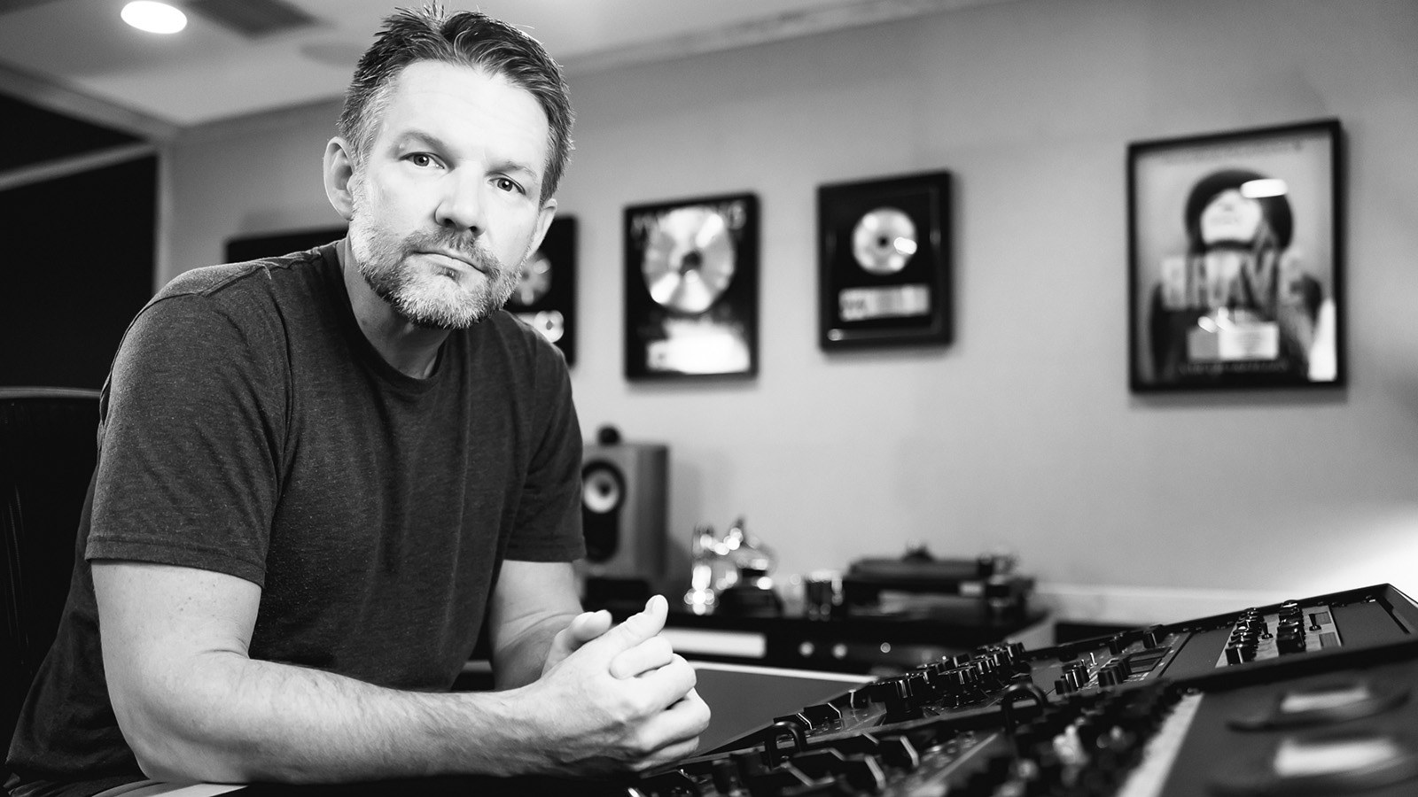 Brad Blackwood sits at an audio console in a studio with framed gold records on the wall behind him.