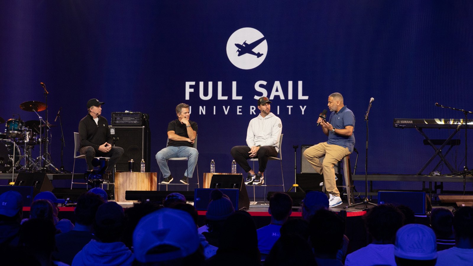 MLB Pitcher Adam Wainwright and three other people are seated on a stage during a panel, the large-scale LED screen behind them reads “Full Sail University” against a blue backdrop.