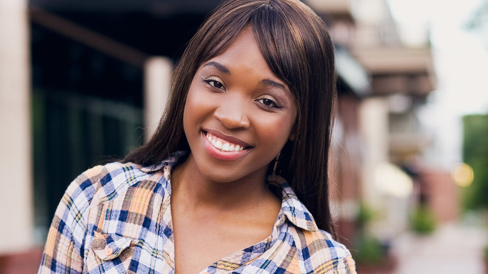 Brandie Green smiles at the camera. She is standing outdoors and wearing a flannel button-down shirt.