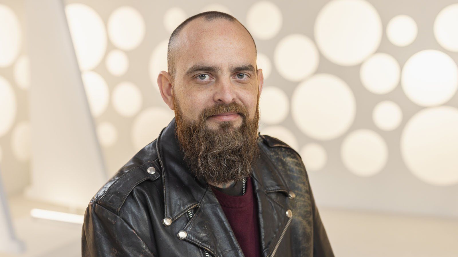 Full Sail Hall of Fame inductee Ben Rice smiles at the camera. He is wearing a burgundy sweater and a black leather jacket.