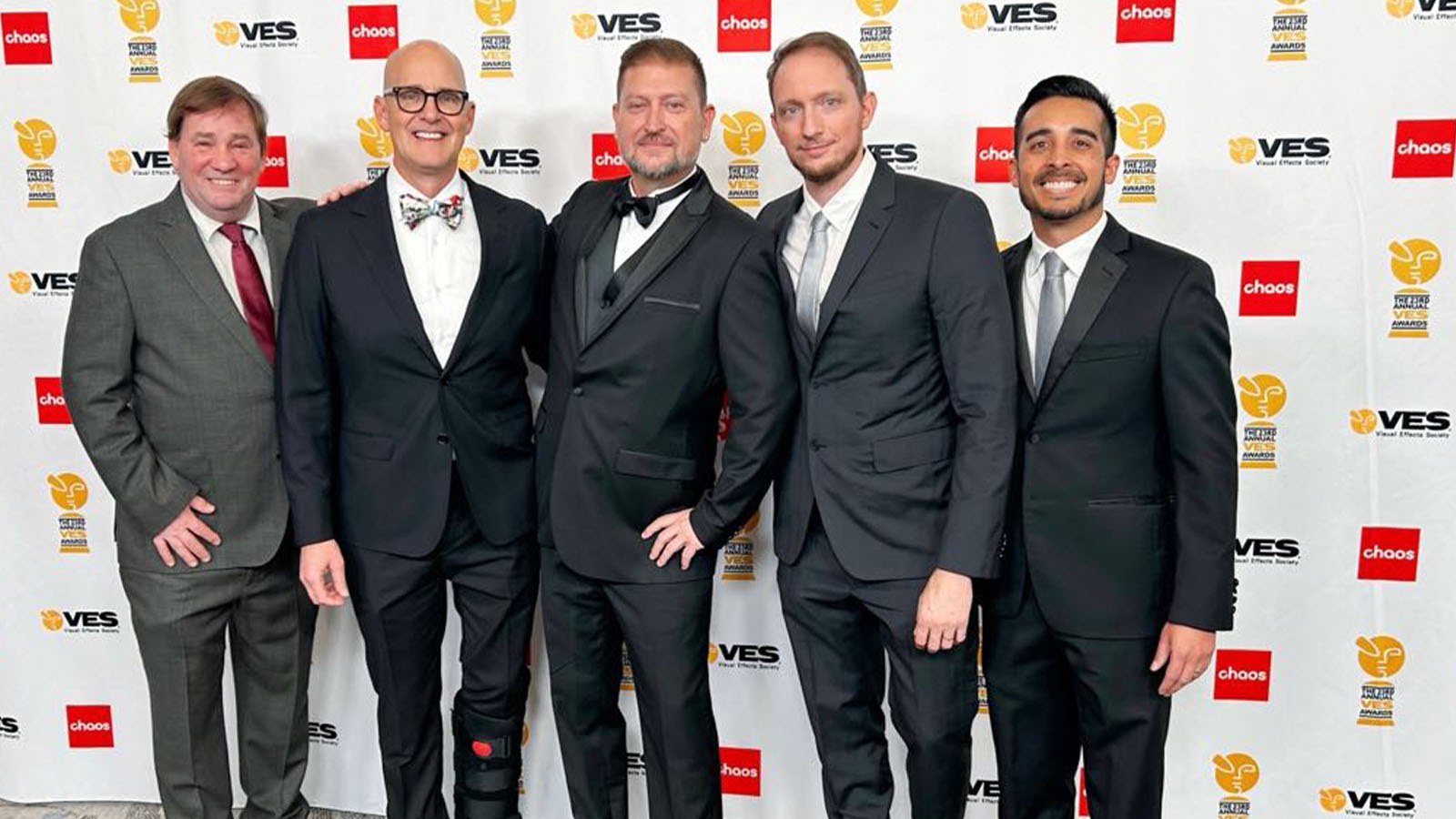 Culley Bunker stands with four special effects artists from Skulley FX in front of a VES Awards backdrop. They are wearing suits and smiling.