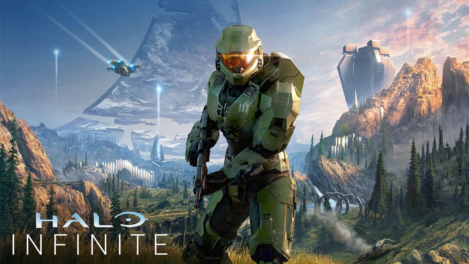 Halo main character Master Chief in signature green armor featuring the number 117 on his left chest plate in white, centered in front of a large grey triangular space ship with the words ‘Halo Infinite’ stylized in the bottom left corner.