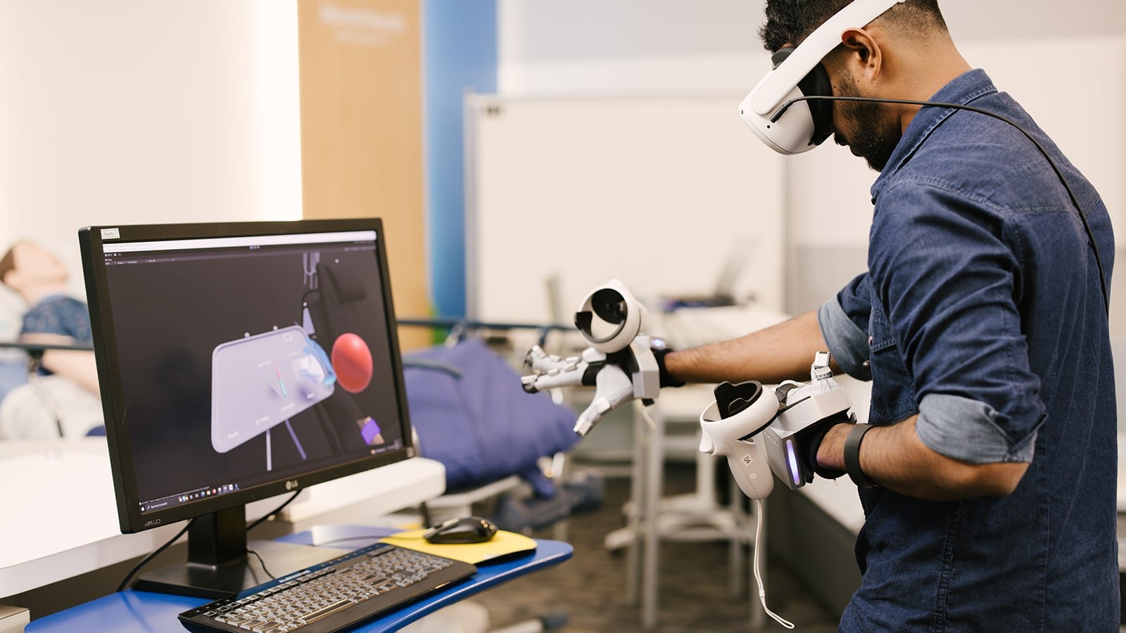 A man in a navy blue button down shirt wearing virtual reality gear on his head and heads while interacting with a screen in front of him.