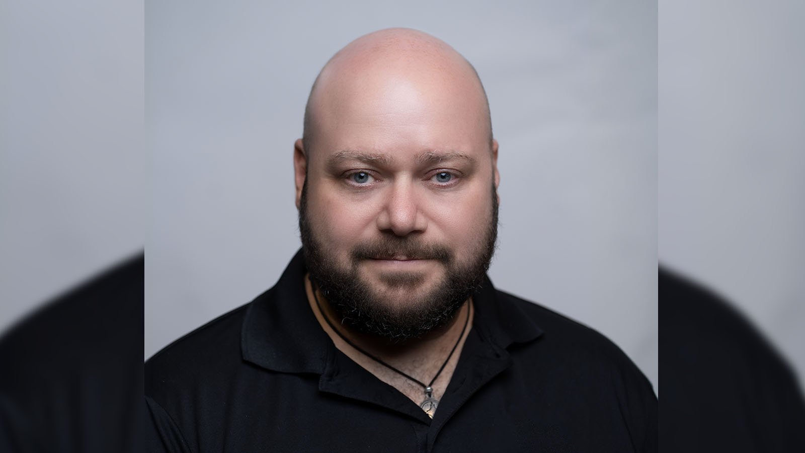 Grad Corey Guerra is wearing a black polo shirt and posing for a headshot against a light grey backdrop.