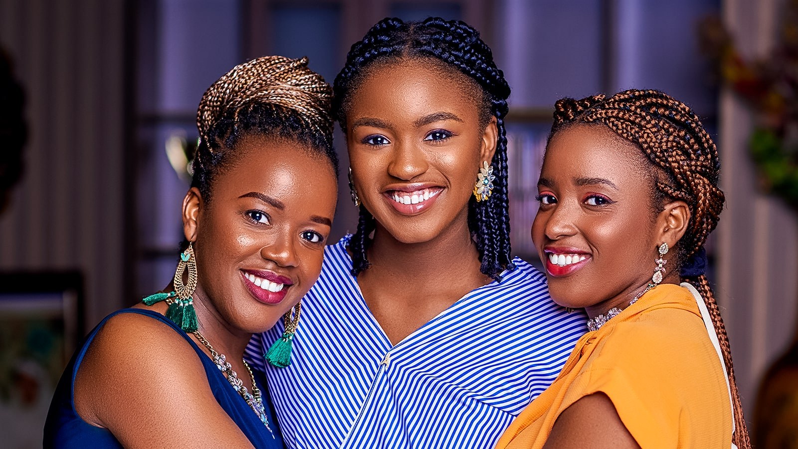 Three sisters, Jemima, Jeiel, and Jesimiel Damina, holding each other closely while posing with bright smiles.