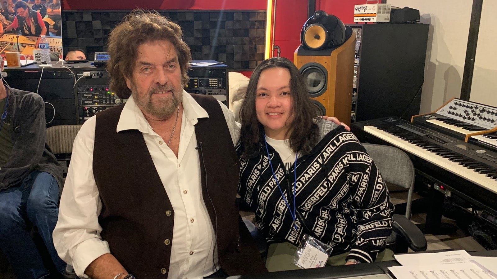 Alan Parsons sits with Steffie Tjandra in front of a mixing board in a recording studio. They are smiling at the camera.