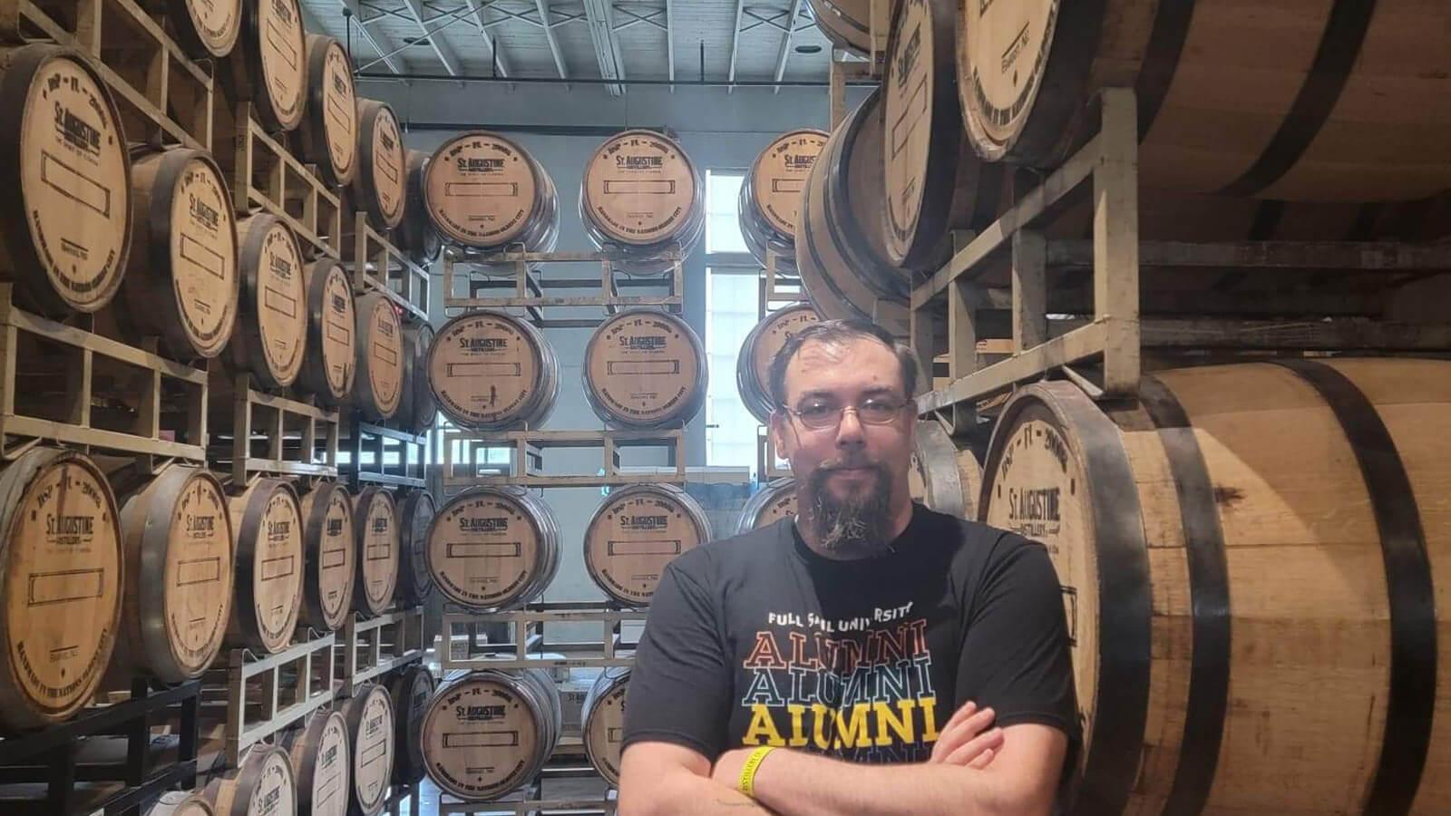 Daniel Vanallen sits in a chair at St. Augustine Distillery Co. He is smiling and wearing a Full Sail Alumni shirt.
