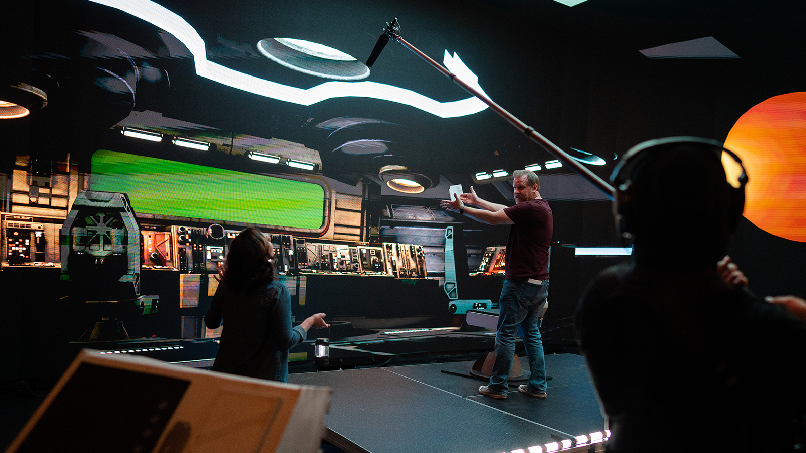 Space Pups’ director Jason Murphy stands onstage in a virtual spaceship set. He is talking to a crew member while another crew member holds a boom mic.