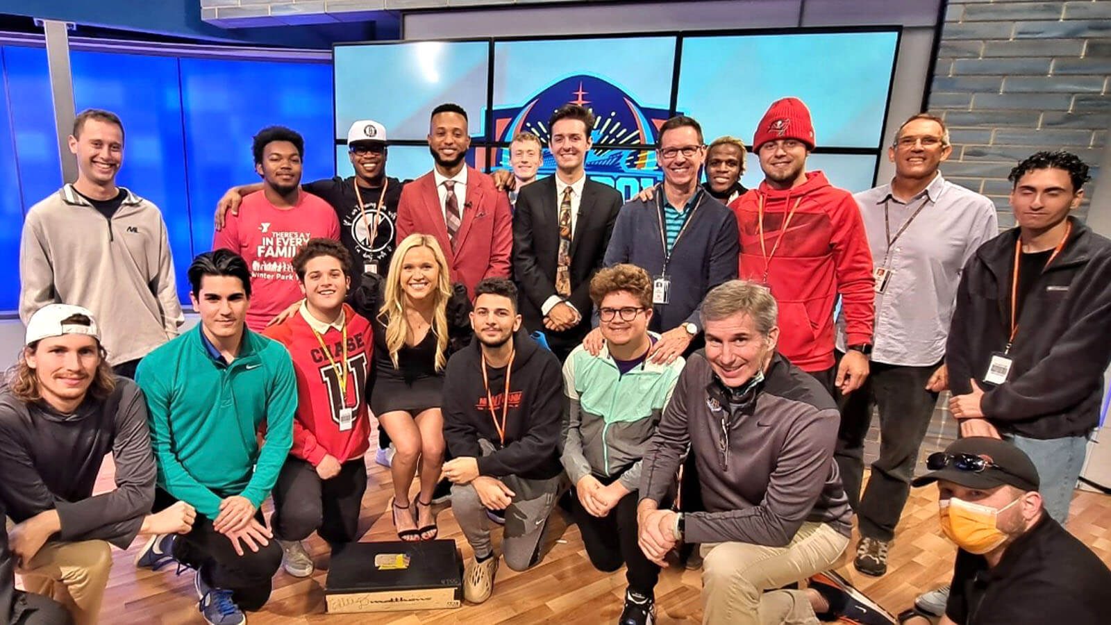 A group shot of several Full Sail students and instructors in front of a large screen on set at the Dan Patrick School of Sportscasting.