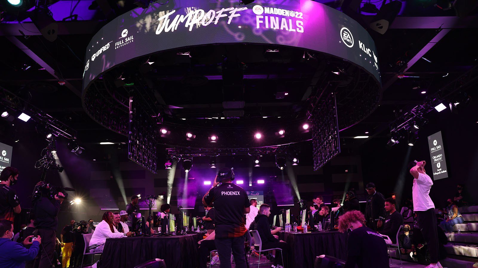 The Full Sail University Orlando Health Fortress esports arena’s main stage and large screens feature Jump Off’s purple and white branding while competitors face-off at gaming stations.