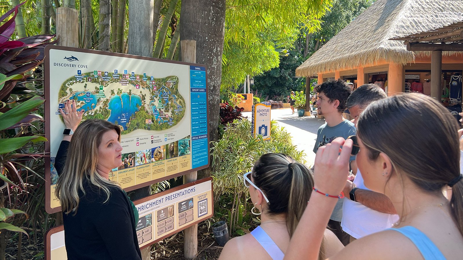 Crystal O’Hea stands at a map of Discovery Cove and speaks to students as they stand around.