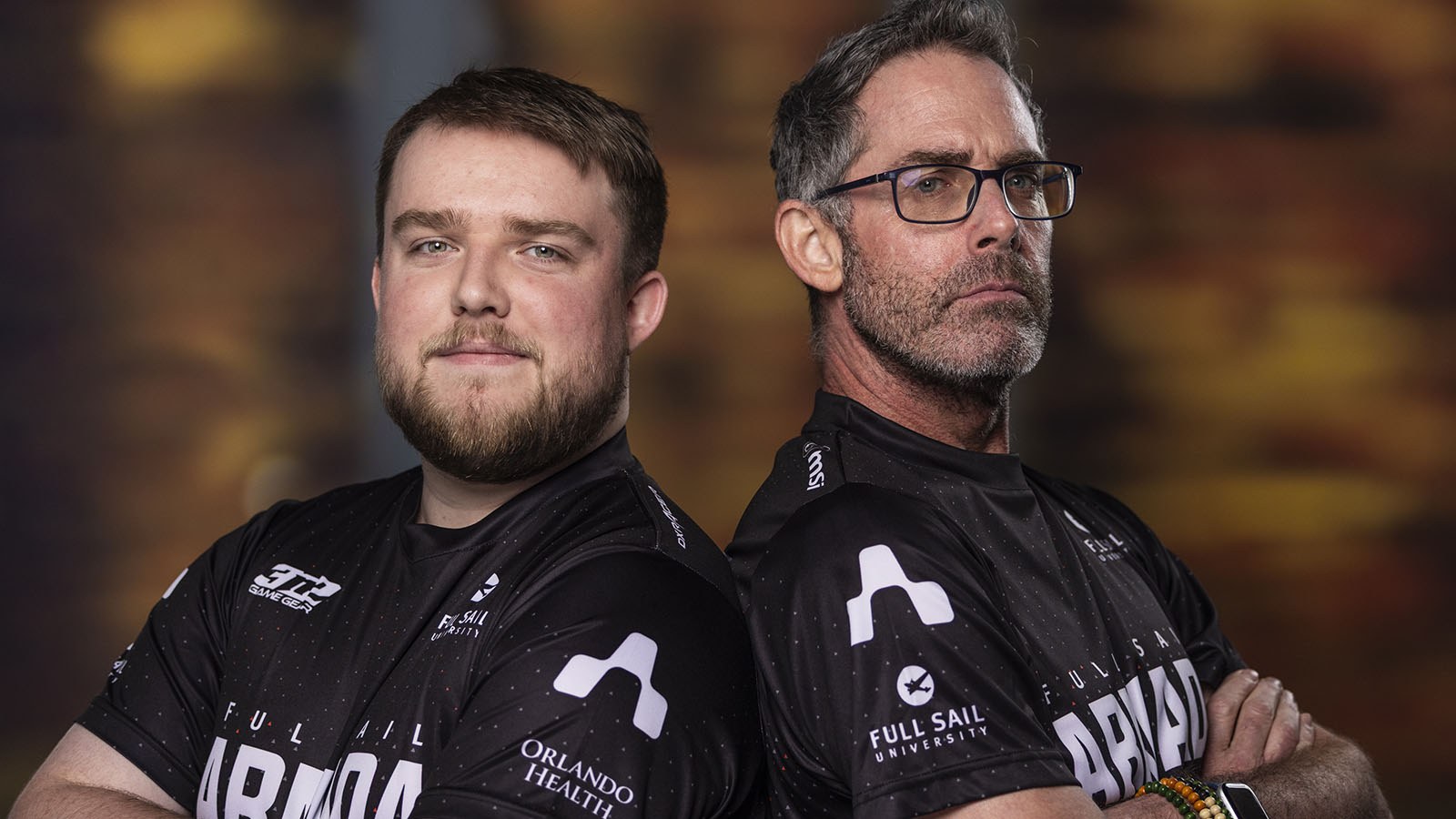 Full Sail Armada staff members Garrett Gajewski and Chris MacMillan stand back-to-back with their arms crossed. They are wearing black and white Armada jerseys.