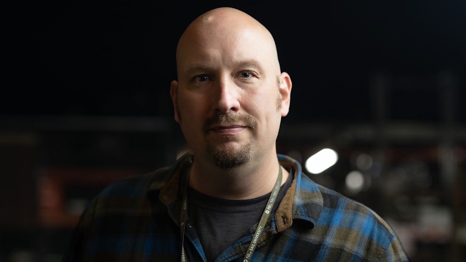 Headshot of Andrew Garraway wearing a blue and grey plaid flannel and a Full Sail lanyard, complete with Full Sail pins.