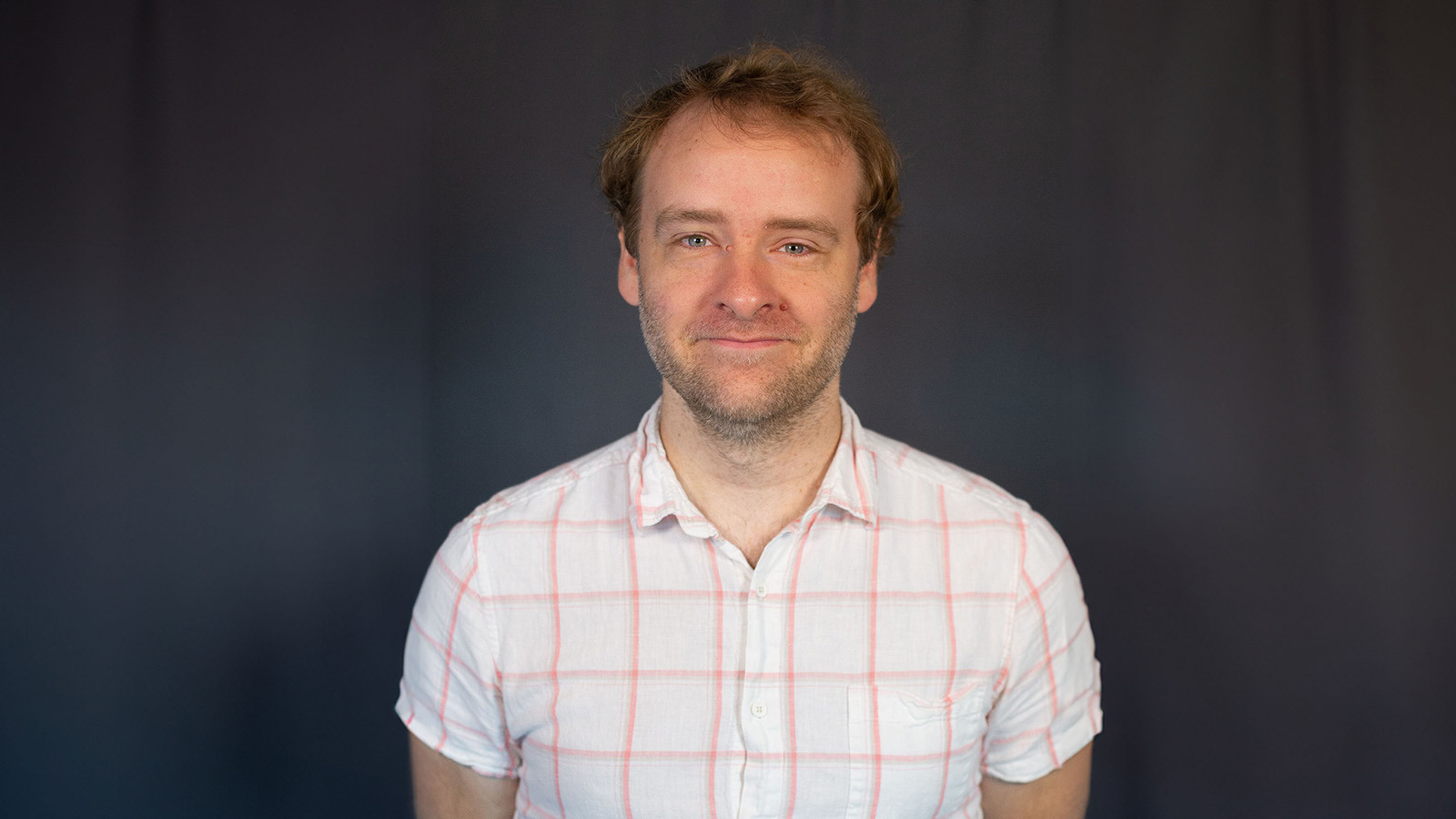Paul Ellison smiles at the camera. He has short blonde hair and blue eyes and is wearing a white and red button-up shirt.