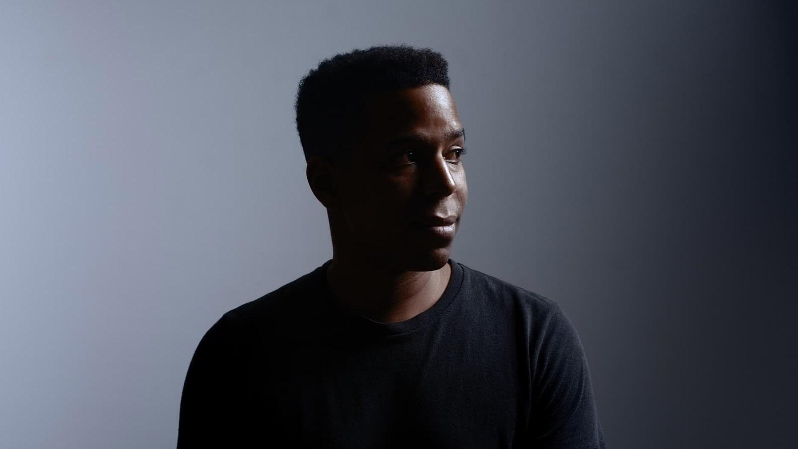 Dylan Coleman sits against a gray background and looks off to the side. He’s wearing a black t-shirt.