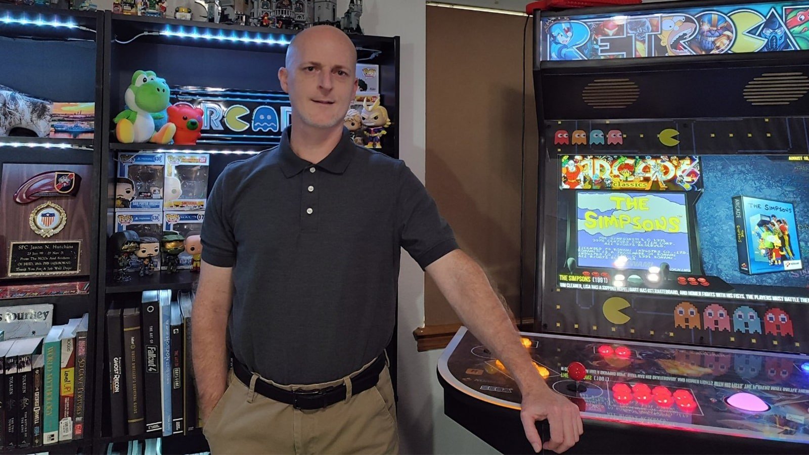 Jason Hutchins standing next to an arcade machine while wearing a blue polo and tan slacks.