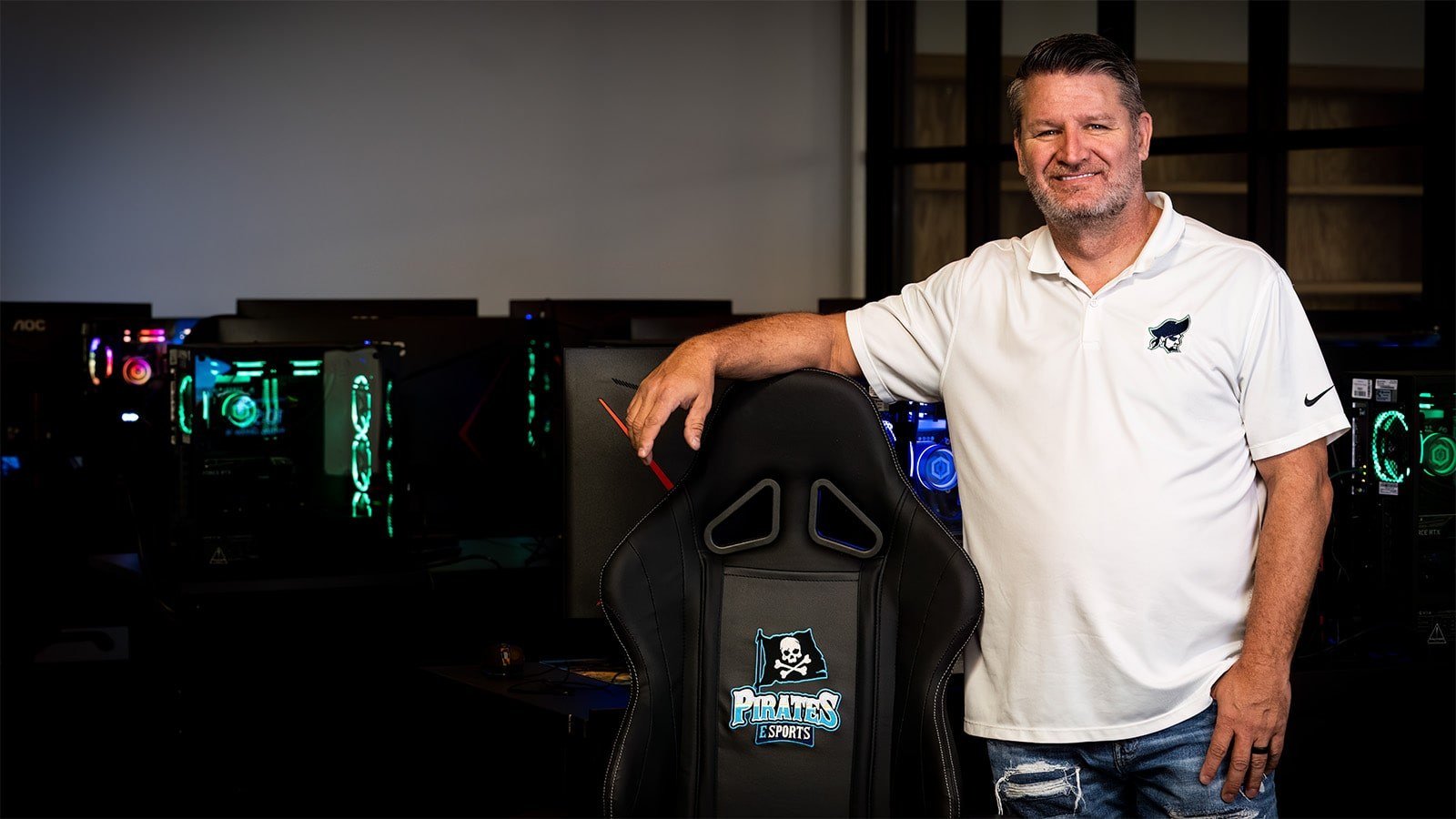 Scott Brumfield stands in front of gaming PCs. He is next to a PSC Pirates gaming chair and is wearing a Pirates shirt.