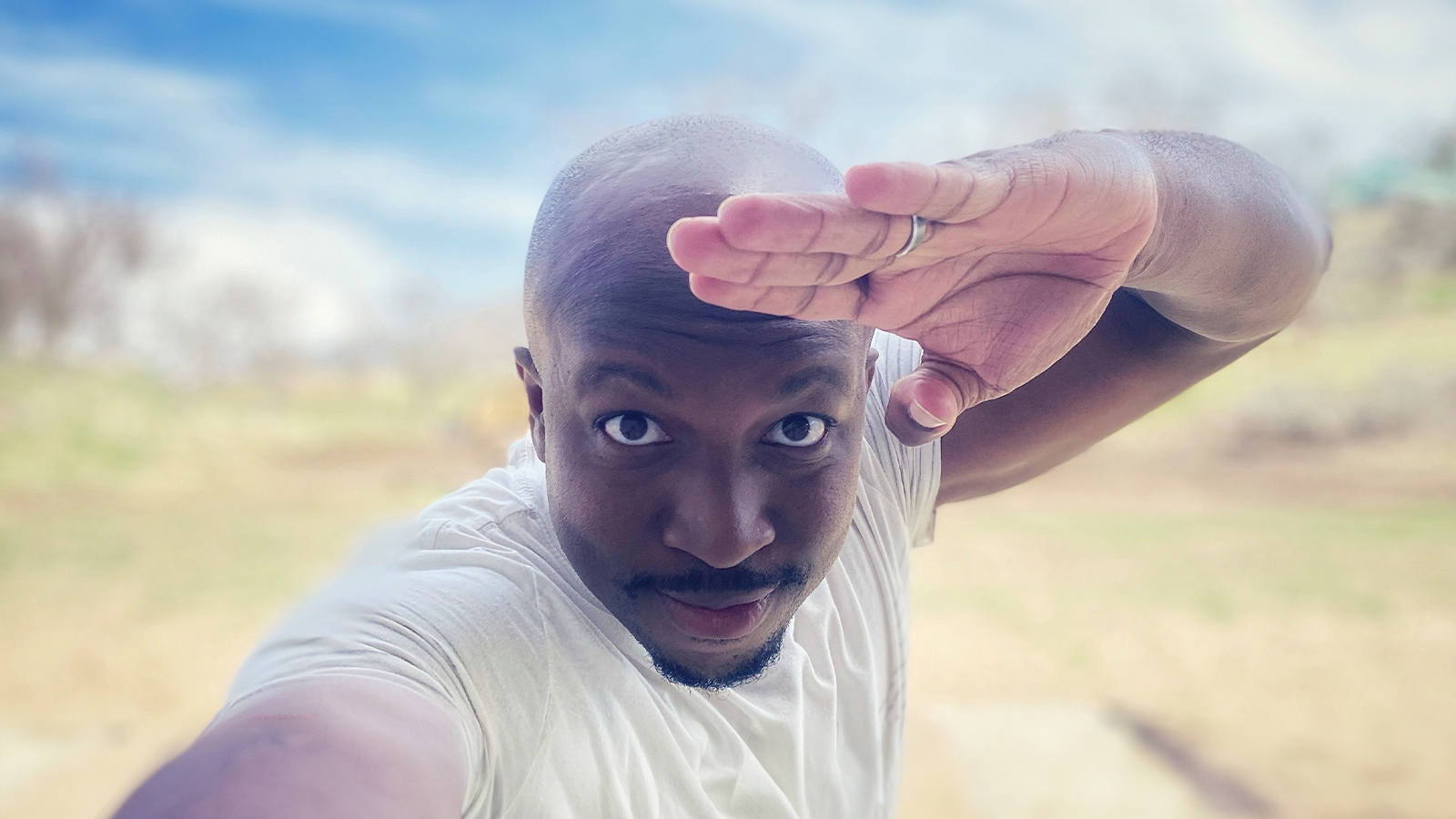 Chancler Haynes stands outside on a sunny day. He is wearing a white t-shirt and saluting at the camera.