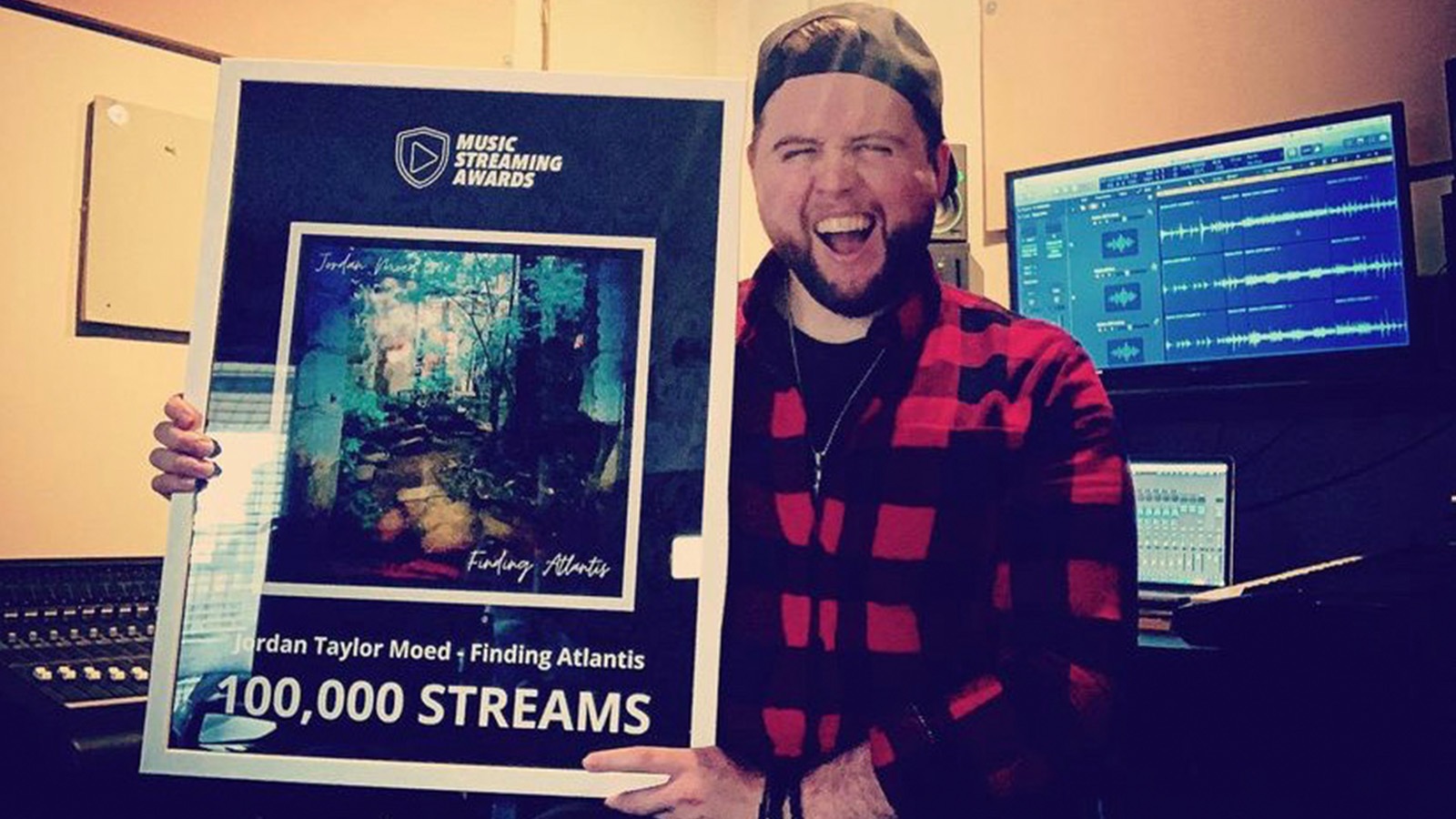 Jordan Moed stands in his studio and holds an award for 10,000 streams for his song “Finding Atlantis.”