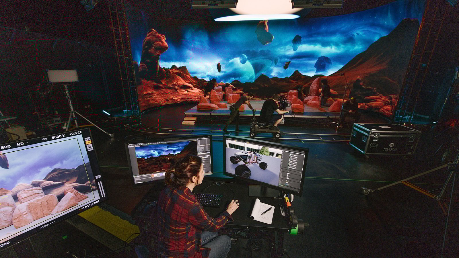 A production crew films on a sci-fi virtual set while a technician controls digital environments on monitors.