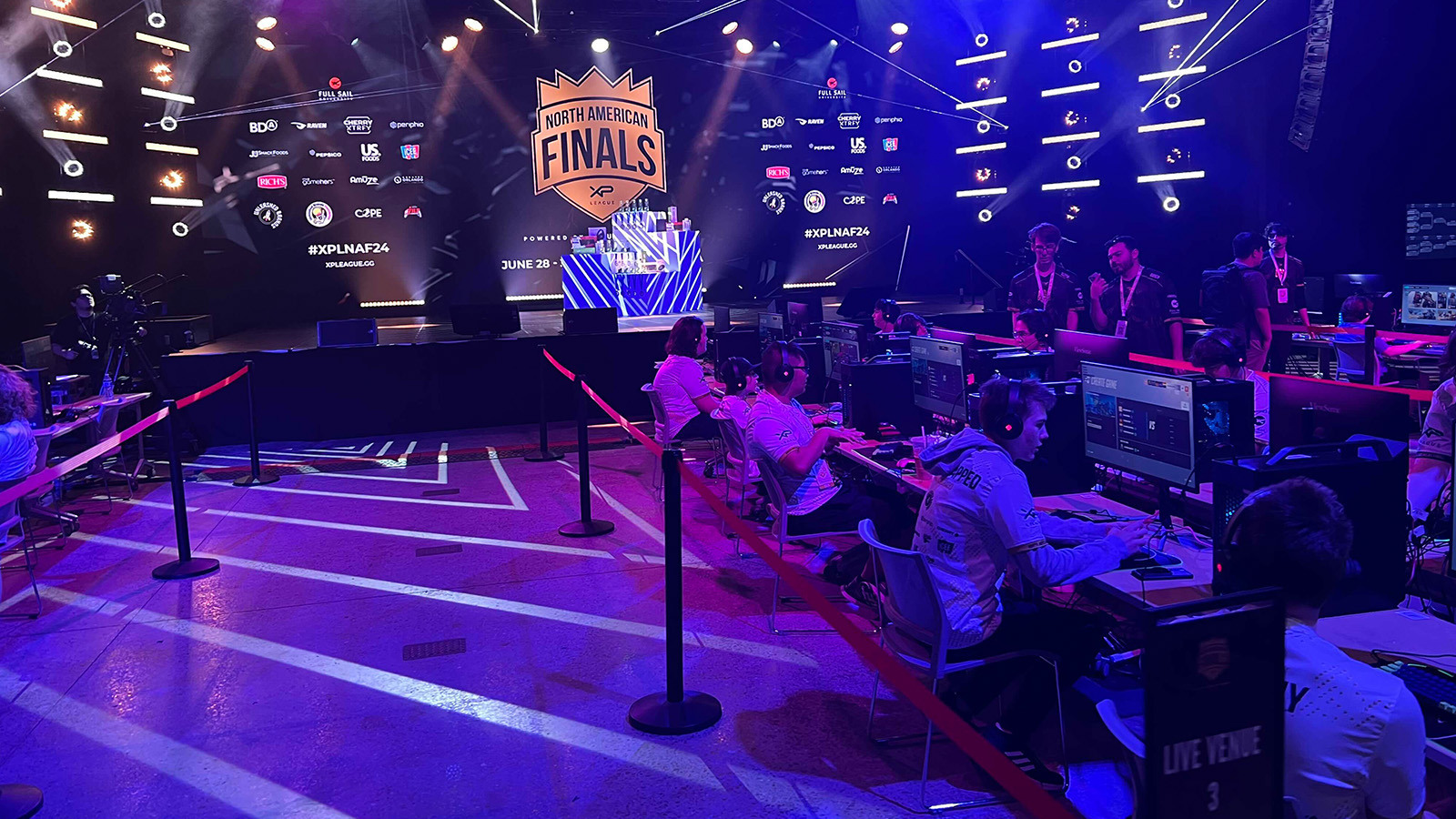 The stage in Full Sail’s Live Venue appears in the background of a row of players seated at gaming stations during the XP League North American Finals.