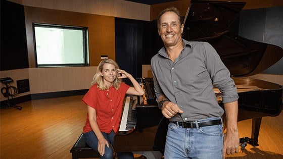 Aoife O’Donovan sits at a grand piano in Full Sail’s Audio Temple. Darren Schneider leans against the piano.